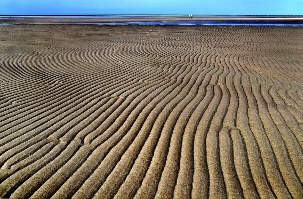 A couple walked along Chapin Beach as patterns formed on the sand at low tide. Image by John Tlumacki. United States, 2019.