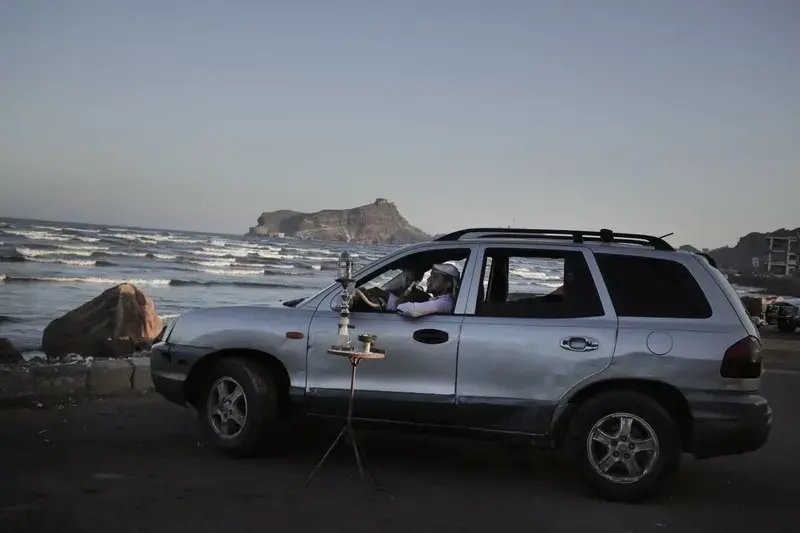 In this Feb. 13, 2018, photo, a man smokes a traditional “shisha” water pipe inside his car parked his car in front of the beach in Aden, Yemen. Even with a civil war in full swing, people seek some simple recreations and acts of normal life. Image by Nariman El-Mofty. Yemen, 2018.<br />
