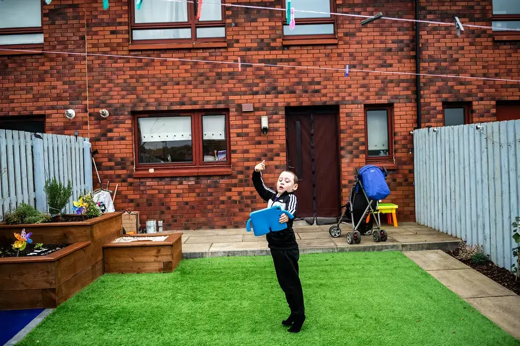 David Crichton plays on his iPad in the backyard of his home, where he has a sensory garden, in Possilpark. Image by Michael Santiago. United Kingdom, 2019.