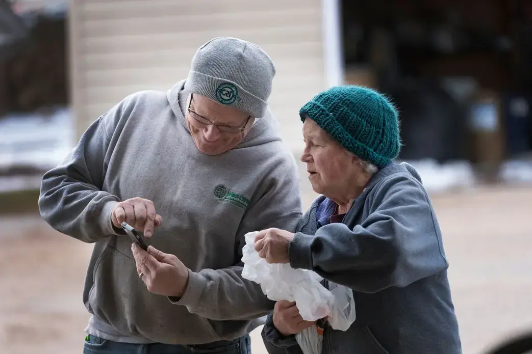 Hans Breitenmoser Jr. shows his mother, Margaret, something on his phone. Breitenmoser, the son of Swiss immigrants, milks about 350 cows on his dairy farm in Merrill in Lincoln County. Image by Mark Hoffman. United States, 2019.