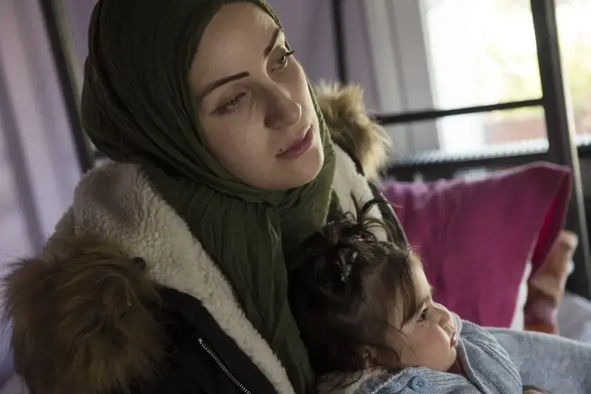 Syrian refugee, Taima, prepares to take her 6-month-old daughter, Heln, for a visit to the Acropolis, while her husband, Muhannad Abzali, 28, jokes around with their other child, Wael, 3. Image by Lynsey Addario. Greece, 2017.
