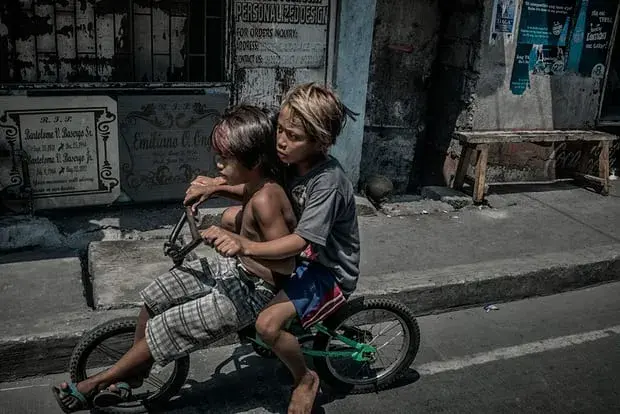 Young boys ride past a tombstone engraving shop on in Navotas. Image by James Whitlow Delano. Philippines, 2018.