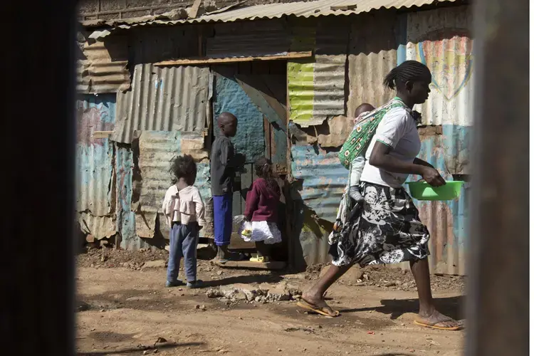 A woman with child on her back carries a wash basin in the Kawangware slum in Nairobi, Kenya. Image by Mark Hoffman. Kenya, 2017. 