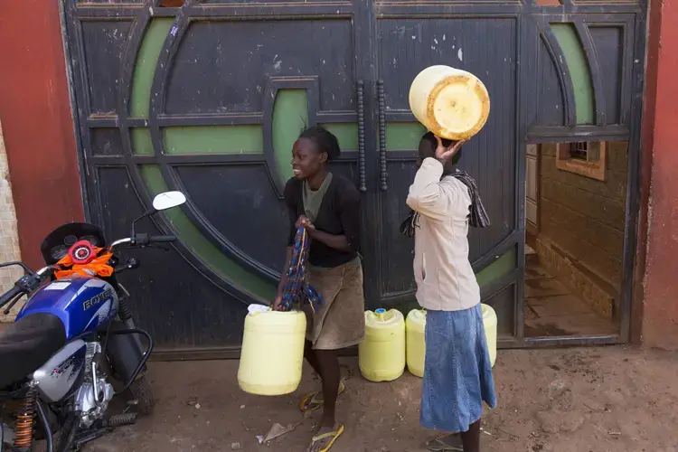 Women carrying containers walk to a merchant who sells drinking water in the Kawangware slum in Nairobi, Kenya. Many of Nairobi's people live in slums and have limited access to clean drinking water and proper sanitation. Image by Mark Hoffman. Kenya, 2017. 