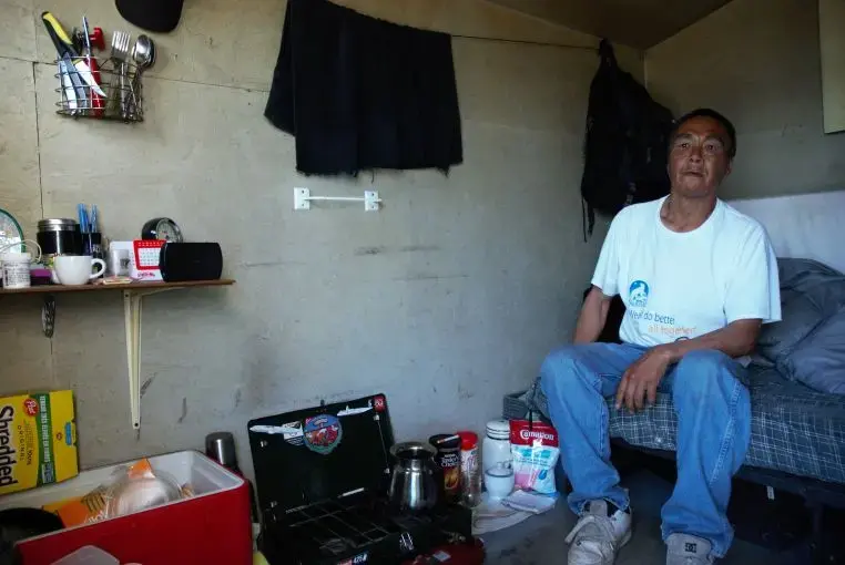 Nushupiq Kilabuk wears a “Nunavut, we do better all together!” t-shirt as he sits in the beachside shed he shares with his wife in Iqaluit. Image by Julie De Meulemeester. Canada, 2018. 