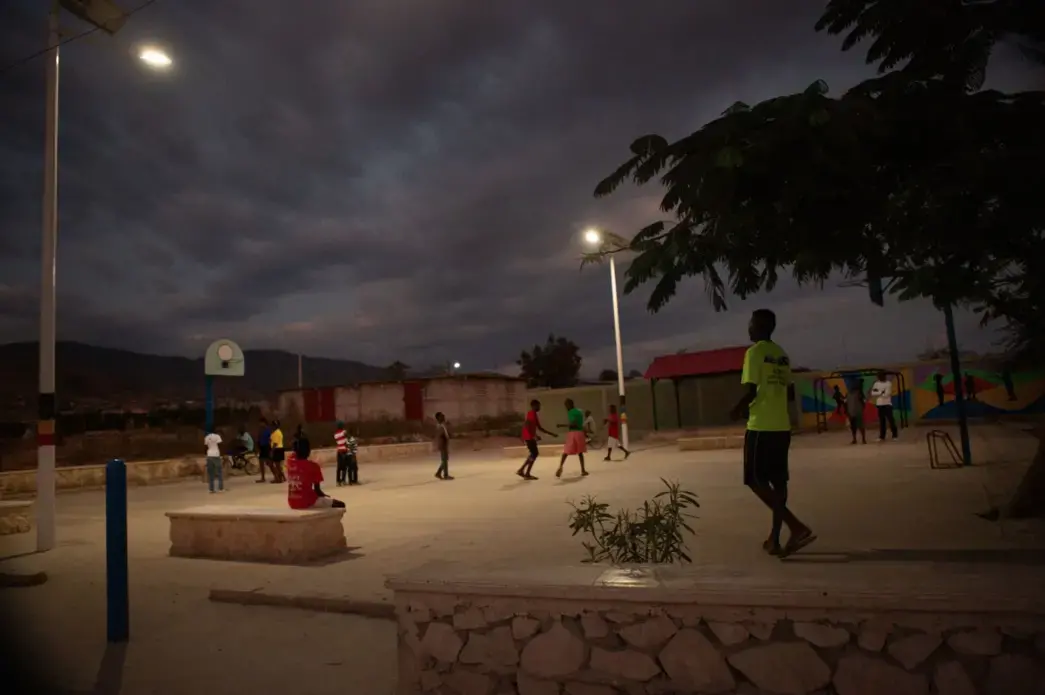 Young men exercise after dark in the recently completed public plaza in the Canaan 1 neighborhood. The community fought hard to keep the land a park after a Haitian man living in Miami tried to claim it as his own, surrounding it with fencing in preparation for building a private home. The park improvements, funded in part by by the American Red Cross, include solar-powered lights. Image by Allison Shelley. Haiti, 2019.