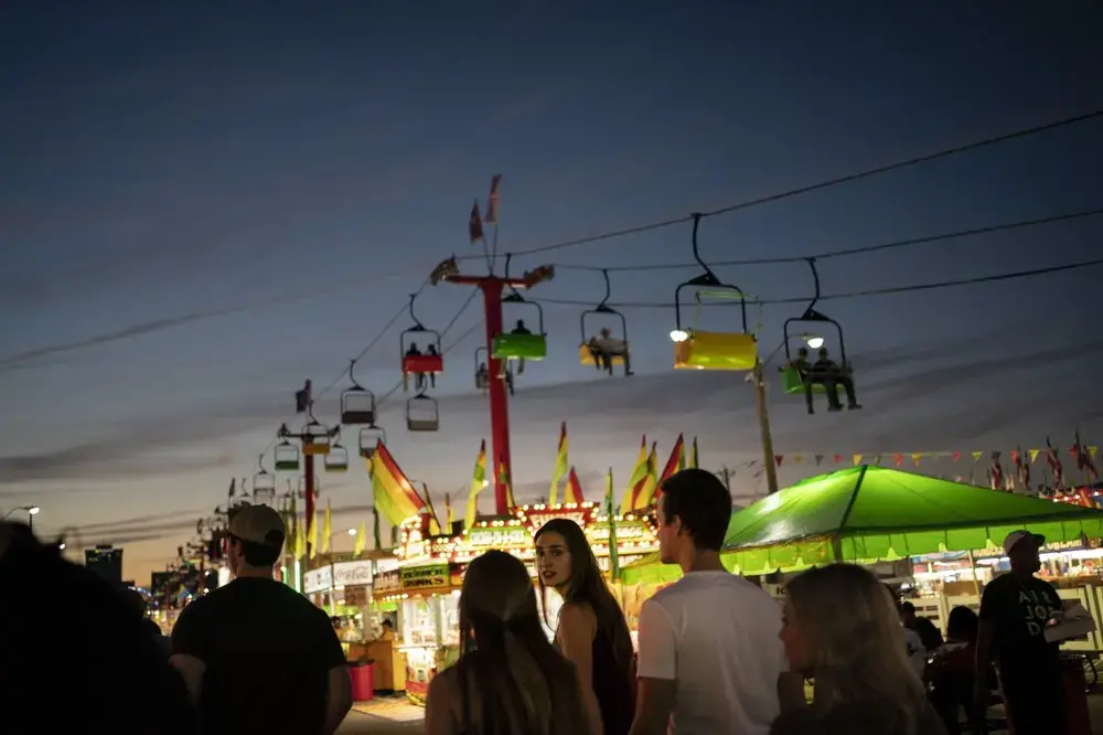 People walk between illuminated booths at the Mississippi State Fair in Jackson, Miss. Image by Wong Maye-E/AP Photo. United States, 2020.