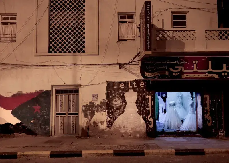 This Feb. 15, 2018, photo shows war damage outside Lelte boutique for wedding dresses on a street in Aden, Yemen. Despite the country’s ongoing war, wedding boutiques are open late into the night, salesmen inside chewing stimulant qat leaves to pass the time. “Women come in and look at some dresses, but they are expensive for people now, so it’s hard to sell,” said one clerk. Image by Nariman El-Mofty. Yemen, 2018. </p>
<p>