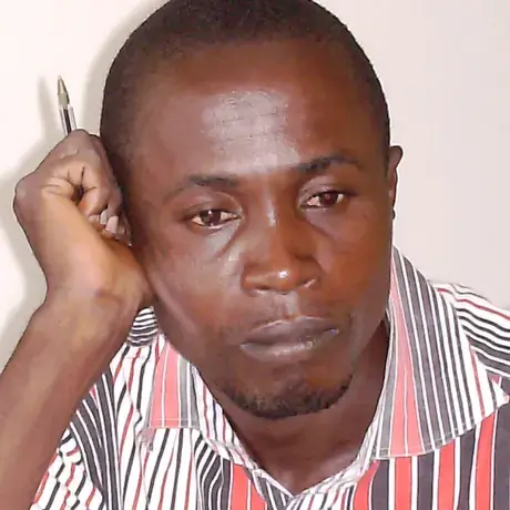 A person wears a red and white patterned shirt. The person is also holding a pen.