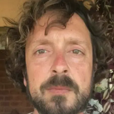 A man wears a white shirt and has brown curly hair.