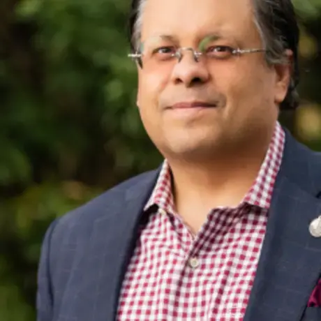 A man wears glasses, a red flannel shirt, and a jacket