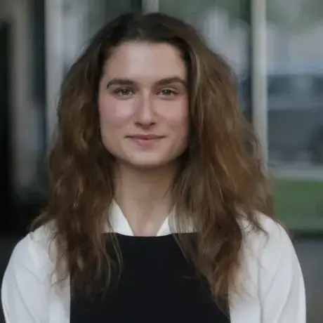 A woman with long light hair wears a white shirt with black overalls