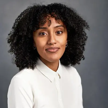 A woman with dark curly hair wearing a white button down shirt