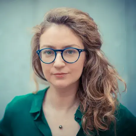 A woman with wavy blond hair and glasses wearing a green button down shirt