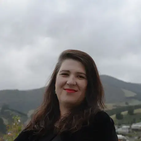 A woman with long dark hair smiles against a mountainous background