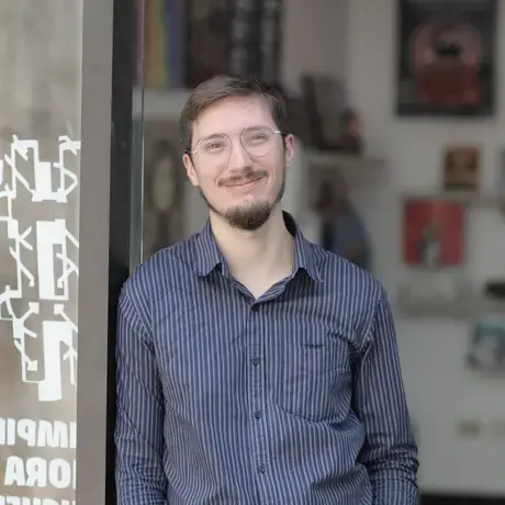 a man with short dark hair, short beard, and glasses wearing a blue button down