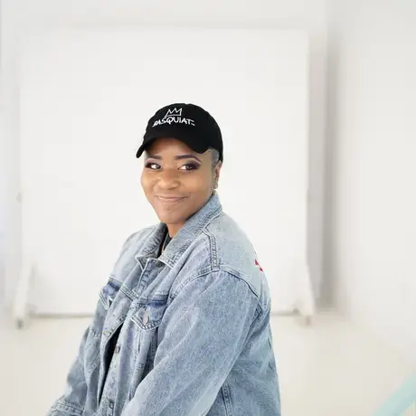 A woman wearing a black "Basquiat" baseball cap and a jean jacket