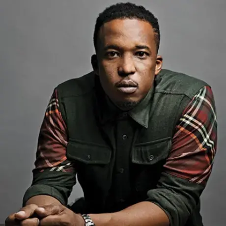 A man wearing a green and plaid button down against a grey background