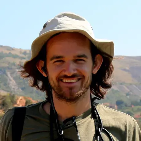 A man with brown hair wearing a tan safari hat and green shirt