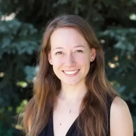 A woman with long brown hair wearing a black top standing against a tree