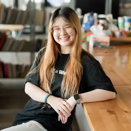 Pitshaya wearing a black tee leans back on a table and smiles into the camera.
