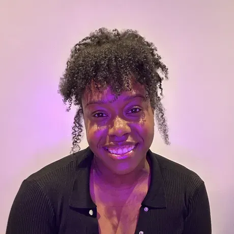 Shauntice, a Black woman with her curls in an up-do smiles at the camera