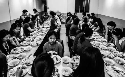 Close to 40 men and women sit around a table and share a meal inside the kitchen of the shelter.