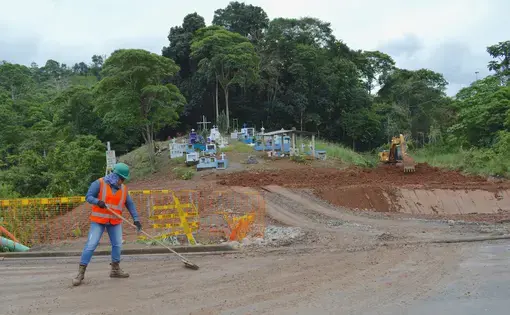 A construction worker on a dirt road at the bottom of a hill with a small cemetery.