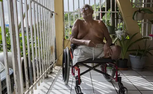 José Maldonado looks out into his neighborhood while seated in his wheelchair on the front porch of his Humacao, Puerto Rico home. Image by Ryan Michalesko. Puerto Rico, 2017.