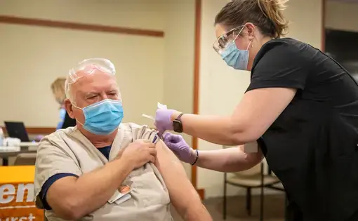 Register Nurse and Infectious Control Specialist Sarah Czechowicz administers the first COVID-19 vaccine at Elmhurst Hospital to Edward Sulita a Transporter at the Hospital on December 12, 2020. Image by Manuel Martinez / WBEZ. United States, 2020.