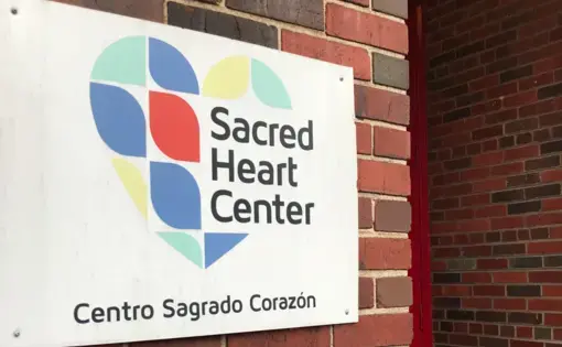 A bilingual sign at the Sacred Heart Center, welcoming all those who enter the community building. Image by Jack Sims. United States, 2019.