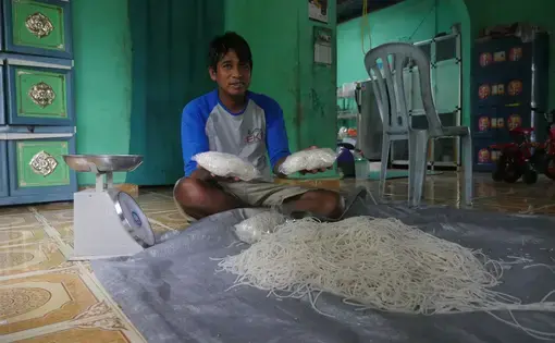 Abdul Manan makes sago noodles with a small pasta maker and packs them for retail sale in plastic bags. He sells about one ton of pasta each month. Image by Daniel Grossman. Indonesia, 2019.