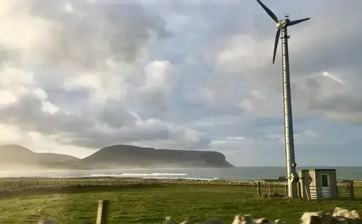 A wind turbine on a farm on the Orkney mainland faces one of the smaller islands off the coast. Image by Maggie More. United Kingdom, 2020.