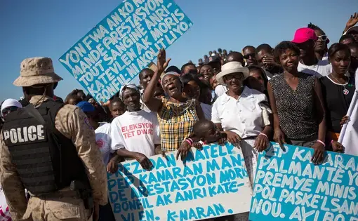 Residents of the former Mozayik tent camp protest at an event attended by Haitian President Michel Martelly commemorating the five-year anniversary of the 2010 earthquake, at the St. Christophe memorial, in Canaan, Haiti. The group of 126 families has been evicted from a tent camp and now from land they bought title to in Canaan. Their signs ask the president to arrest the men who sold them the questionable title. Image by Allison Shelley. Haiti, 2018.