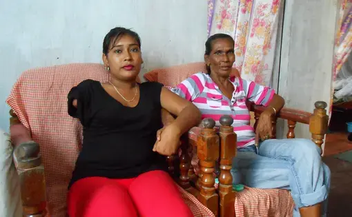 Natasha Houston and her mother at home in Zeelgult. In 2013, Houston's husband killed their two children, slashed her arm and hand, then died, apparently by suicide. Image by William Rawlins. Guyana, 2018.