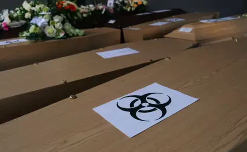 Coffins of COVID-19 victims are marked with a "biohazard" warning sign as they are placed next to each other at the Pompes Funebres Fontaine funeral service company in Gilly, Belgium. Image by Alexandros Michailidis / Shutterstock. Belgium, 2020.
