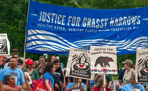 A group of Grassy Narrows First Nation residents and their supporters stand below a "Justice for Grassy Narrows" banner. Members of the Grassy Narrows First Nation traveled to Toronto to demand justice. Image by Shelby Gilson. Canada, 2019.