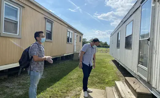 FLOC members Lorenzo Zamora (left) and Braulio Franco (right) wait outside for a farmworker to answer the door during their visit to Liskai Farms migrant camp. Image by&nbsp;Areeba Shah. United States, 2020.