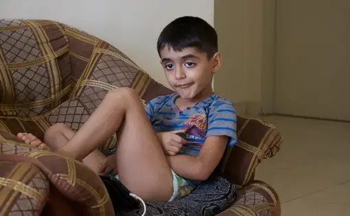 Yahya Al-Zuhairi, a six-year-old autistic boy from Iraq, is sitting on a couch in his home.&nbsp;Image by Ifath Sayed. Malaysia, 2017.