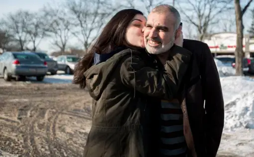 Zahra Ahmad kisses her father, Mohammad Ahmad Sibte, whom she calls Baba, on the cheek before departing to Iraq from Detroit on Feb. 1, 2019. Zahra's parents, Mohammad Ahmad Sibte and Lamiya Adil Mahdi, survived the Irani-Iraqi revolution. Image by Brontë Wittpenn. United States, 2019.