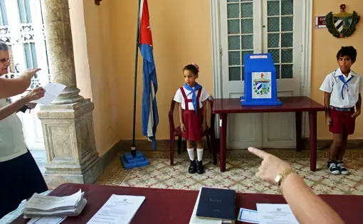 Children wearing the uniform of Communist youth are prepared to salute “Votó!” (“He voted!”), as a woman places her ballot in Cuba’s Elecciones Parciales (Partial Elections). The vote was to elect delegates to the Municipal Assemblies of People’s Power, the country’s unicameral parliament, on April 19, in Havana. The delegates function as district representatives for a two-and-a-half-year term. Image by Yana Paskova. Cuba, 2015.