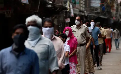 Mobile Covid-19 testing van in India. Delhi Police cop along with people stands in a queue for coronavirus test at Red Zone area, old Delhi. Image by Exposure Visuals / Shutterstock. India, 2020.
