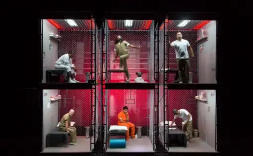 Actors in a multi-level prison cell set on stage during a performance of The BOX.