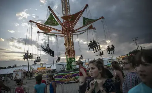 People wait to ride a revolving swing at the Perry State Fair in New Lexington, Ohio, Friday, July 24, 2020. In the towns that speckle the Appalachian foothills of southeast Ohio, the pandemic has barely been felt. Coronavirus deaths and racial protests - events that have defined 2020 nationwide - are mostly just images on TV from a distant America. Image by Maye-E Wong/AP Photo. United States, 2020.