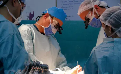 Doctors lean over the operating table, cauterizing an incision on the patient's abdomen, during a kidney transplant performed at the private hospital Clínica Metropolitana, in Caracas. Image by Flaviana Sandoval. Venezuela, 2018.