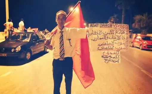 At a protest the evening following a mass beach shooting attack, a Tunisian man in Sousse holds up a banner in French and Arabic condemning ISIL and showing solidarity with the foreign tourists who were targeted. Image by Alice Su. Tunisia, 2015.