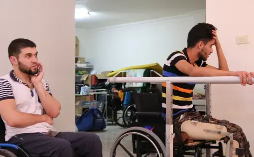 Obada Alasmi sits in on Mohammed Ayyash's training session. Ayyash is confined to a wheelchair,, but they discuss the possibility of using a walker in the near future. Image by Sawsan Morrar. Jordan, 2017.
