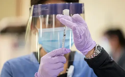 Medical worker in personal protective equipment prepares to administer a vaccine dose. Image by Manuel Martinez / WBEZ. United States, 2020.