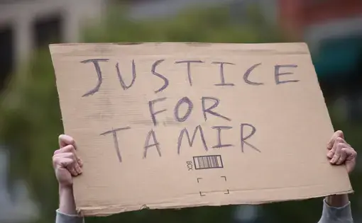 Two hands hold up a cardboard sign that reads "JUSTICE FOR TAMIR."