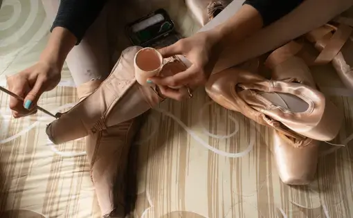 A ballerina uses paint to touch up ballet shoes.